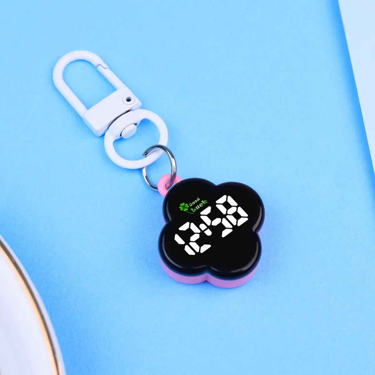 A pink and black LED digital keychain watch with a silver clasp is displayed on a light blue background.