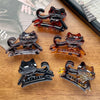 A set of five dark brown and clear acrylic hair clips shaped like cats, displayed on a wooden surface.
