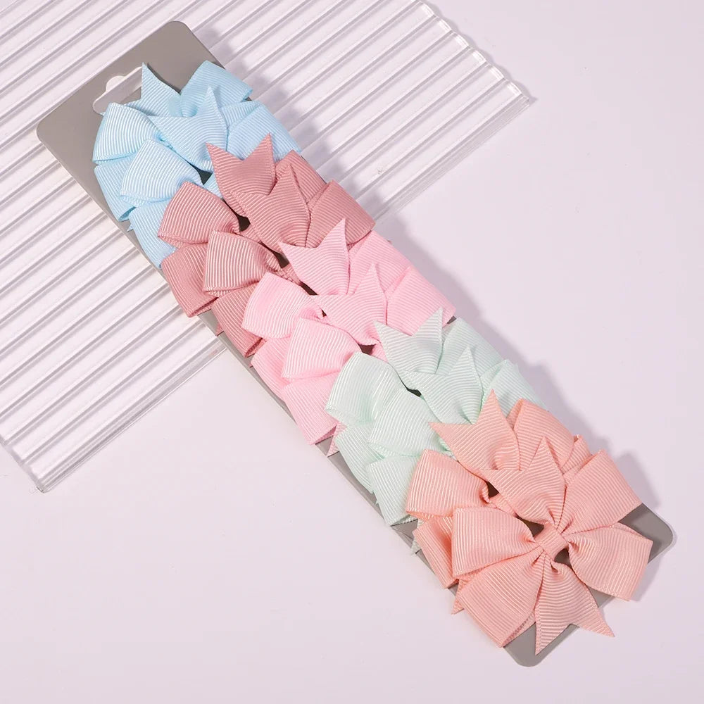 A collection of pink and blue handmade ribbon bow hair clips arranged on a gray card.