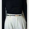 A close-up shot of a white pleated skirt and a black long-sleeved top paired with a thin gold buckle belt.