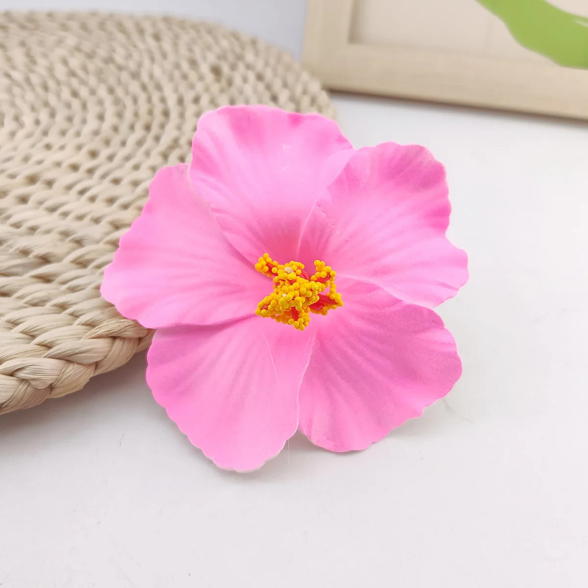 A single bright pink flower with yellow stamens rests on a woven natural fiber background.