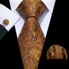 A close-up of a men's silk jacquard tie in gold and brown paisley pattern worn with a white dress shirt.