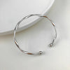 A silver-toned twisted cuff bangle resting on a white surface.