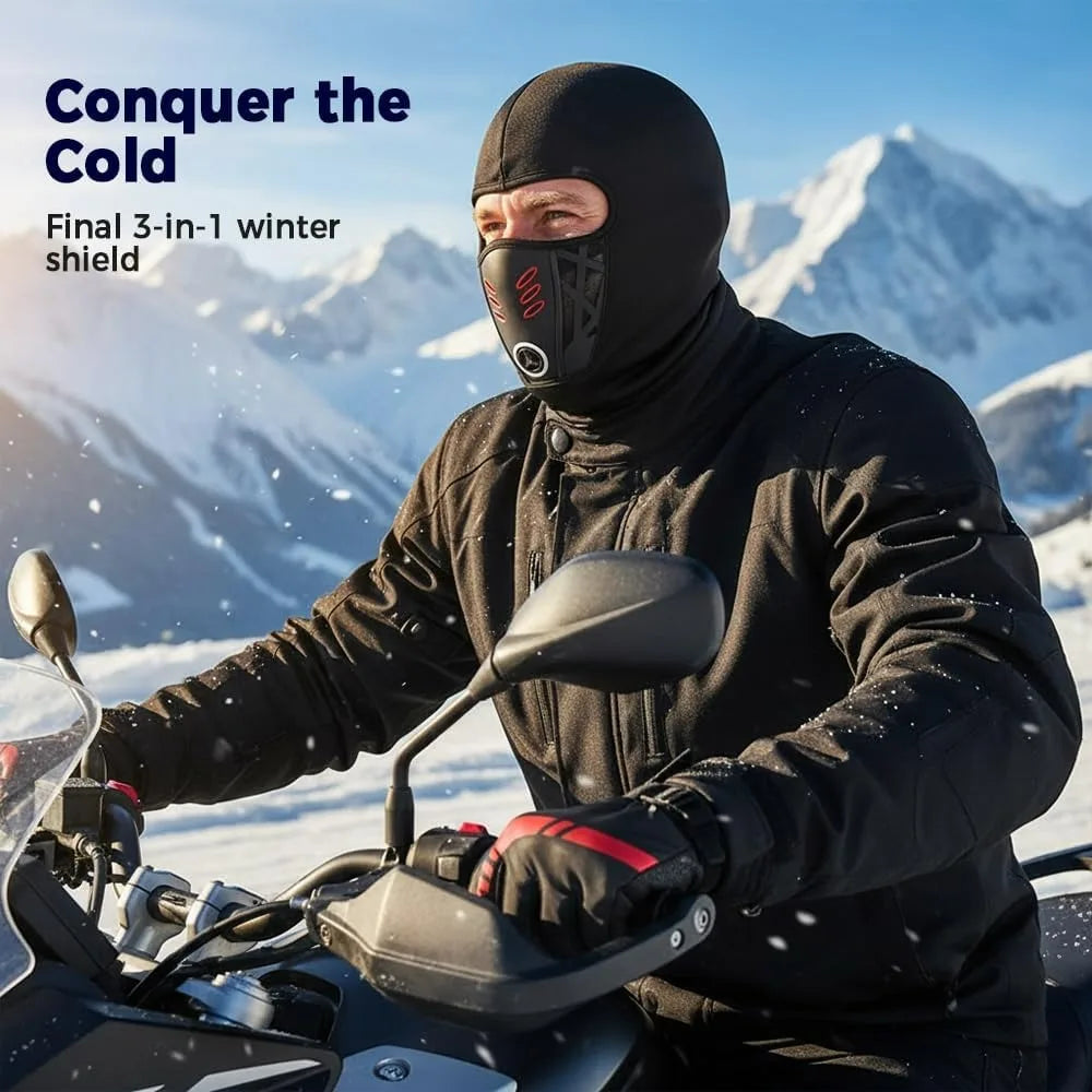A man wearing a black balaclava and jacket rides a motorcycle in a snowy mountain landscape.