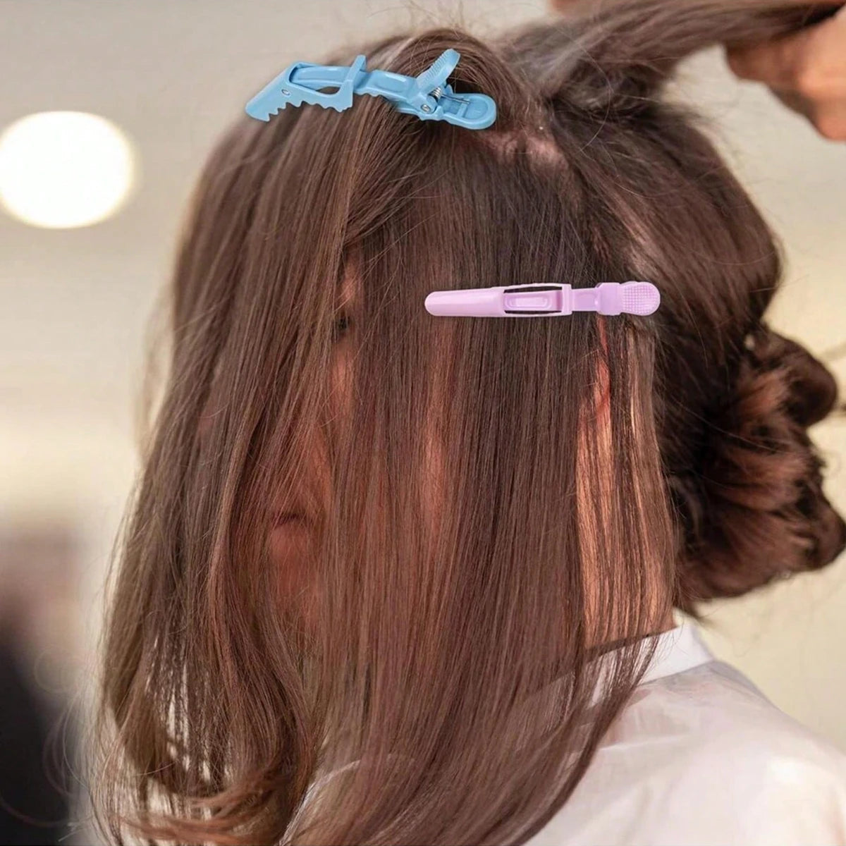 A close-up of a person's hair showing two purple and blue professional multifunctional hair sectioning clips being used for s