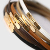 A close-up of several skinny leather belts in brown, tan, and white with gold buckles.