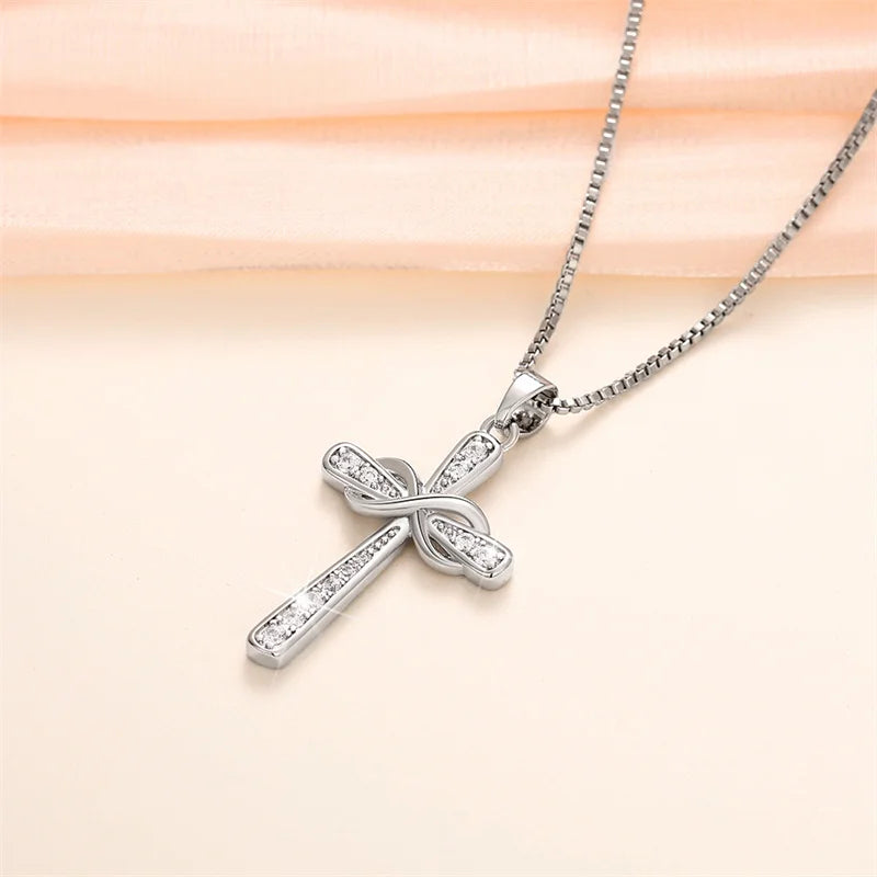 A silver cross pendant necklace featuring a detailed, intertwined design and small diamonds, displayed on a soft peach fabric
