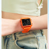 An orange digital wristwatch is worn on a person's wrist, visible against a light green top and denim jeans.