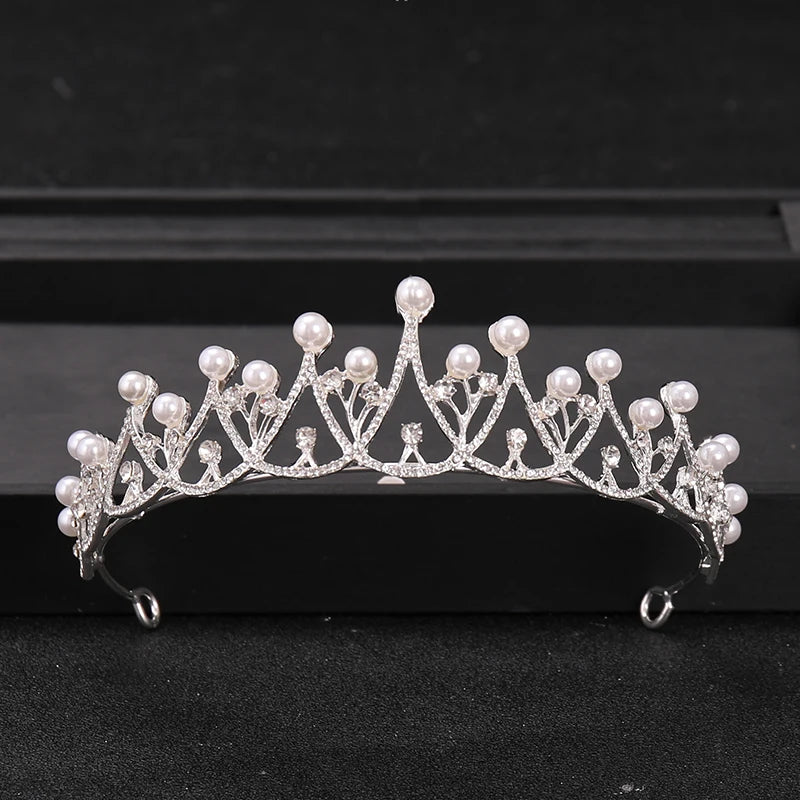 Silver crystal rhinestone bridal tiara headpiece with pearl drops displayed on a black surface.