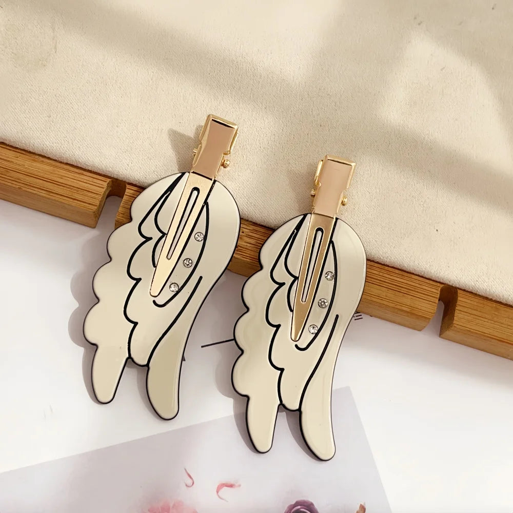 Gold-toned angel wing hair clips and barrettes displayed on a wooden surface.