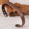 A vintage flower engraved copper bracelet and ring set resting on a light fabric next to a piece of wood.