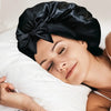A woman is sleeping peacefully with a black satin wide-brimmed hair wrap headscarf on her head.