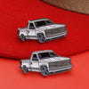 A silver metal clip pin featuring a white pickup truck model on a red fabric background.