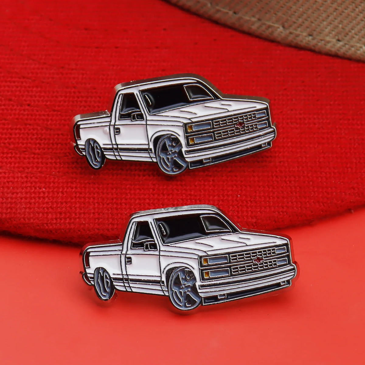 A silver metal clip pin featuring a white pickup truck model on a red fabric background.