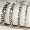 Silver multi-chain stainless steel anklets displayed on a white textured surface.