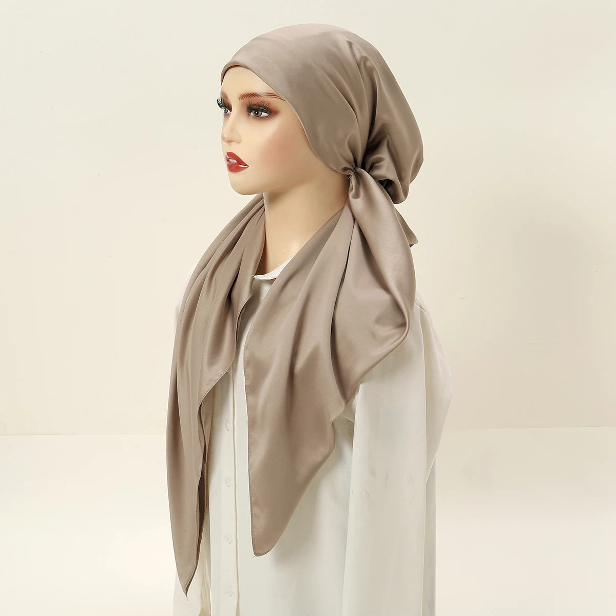 A model wearing a beige satin silk hijab headband cap and white clothing.