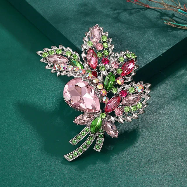 Broche florale en cristal élégante avec des pierres roses et vertes sur un support argenté.