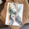 A light blue and green silk scarf tied in a knot, displayed on a beige blazer.