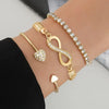 A set of three gold-toned charm bracelets featuring crystal accents and a heart pendant worn on a wrist.