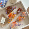 Collection de pinces à cheveux en forme d'octopus colorées, avec des designs irisants et texturés, arrangées dans un plateau 
