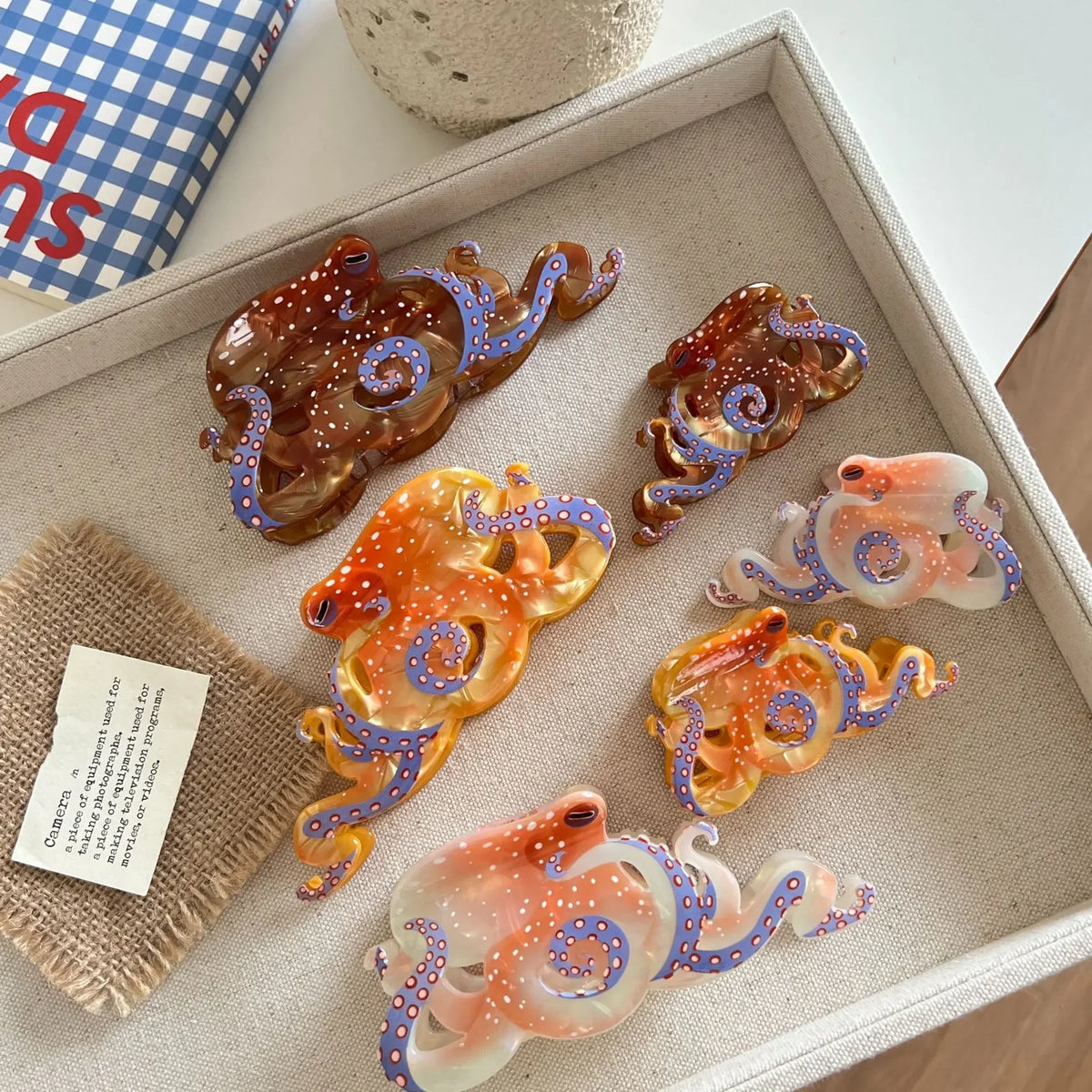 Collection de pinces à cheveux en forme d'octopus colorées, avec des designs irisants et texturés, arrangées dans un plateau 