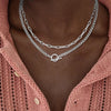 A close-up of a gold layered Cuban link necklace worn around the neck against a pink knitted sweater.