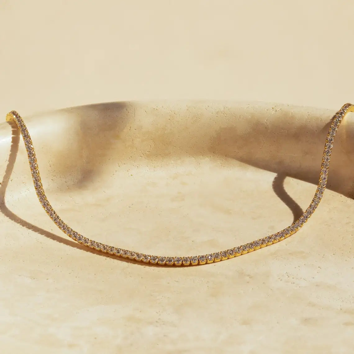 Collar de gargantilla dorado delicado incrustado con pequeñas piedras de circonita de imitación, mostrado sobre una superfici