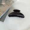 Barreta de pelo negro con lunares blancos sobre una caja transparente.