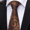 A close-up of a brown patterned silk jacquard tie worn with a white dress shirt and black suit jacket.