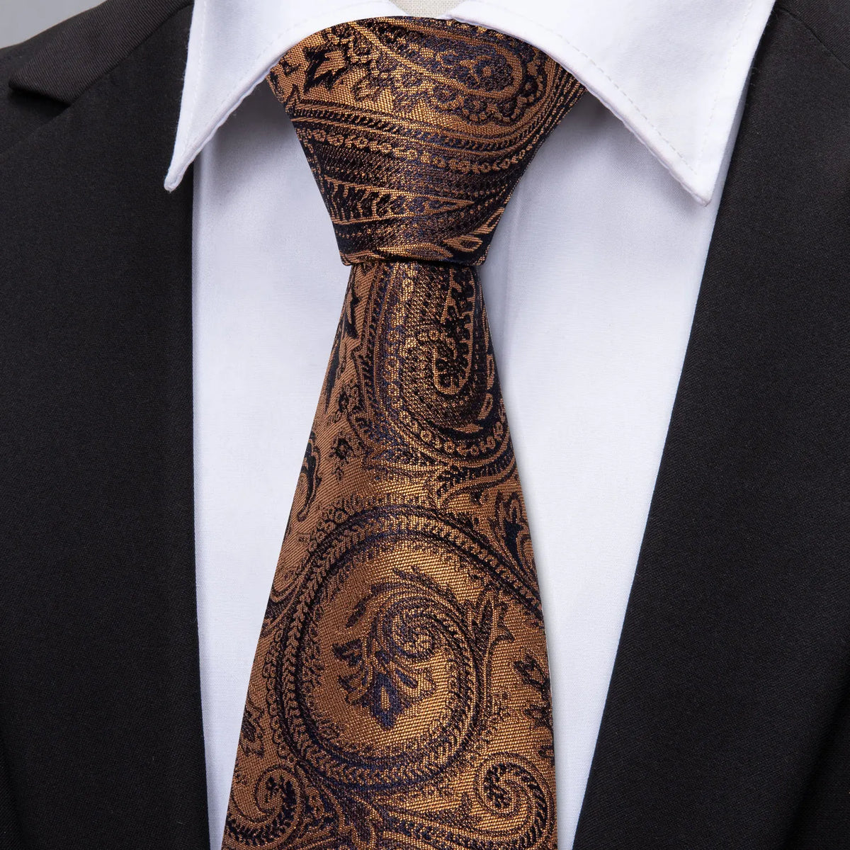 A close-up of a brown patterned silk jacquard tie worn with a white dress shirt and black suit jacket.