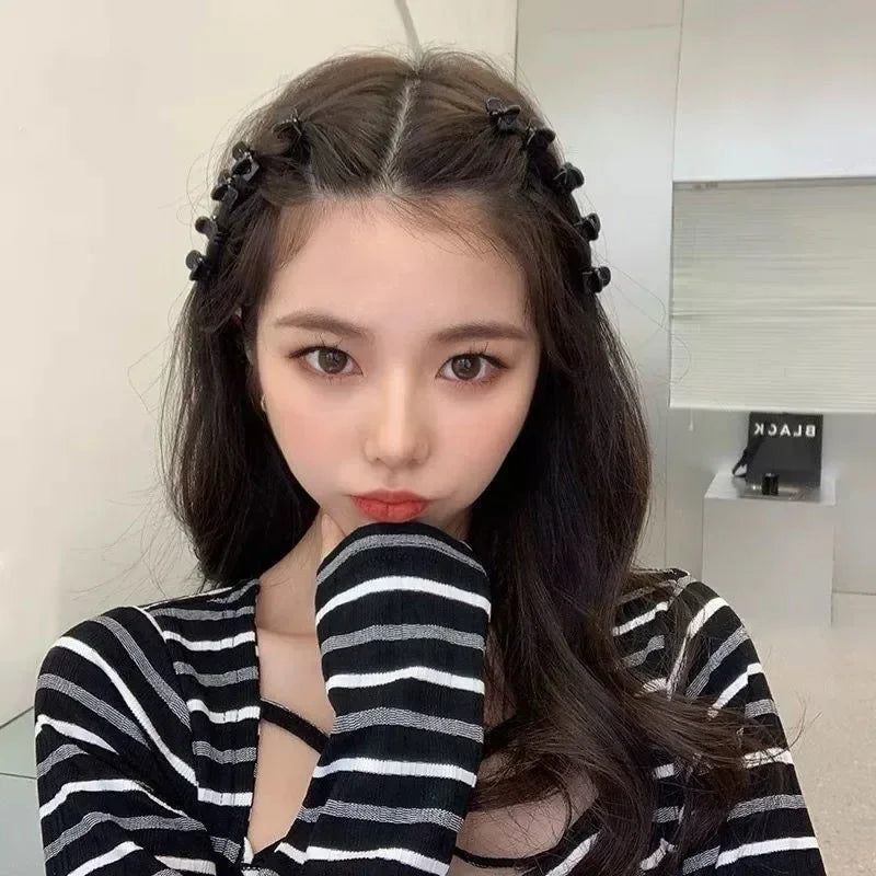 A close-up of a woman with long dark hair wearing a black and white striped top and holding her hair with adjustable hair cla