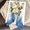 A light beige silk scarf tied in a bow with blue stripes and floral accents, displayed on a white card.