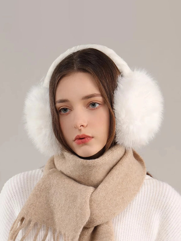 A woman wearing beige faux fur earmuffs and a cream sweater against a neutral background.