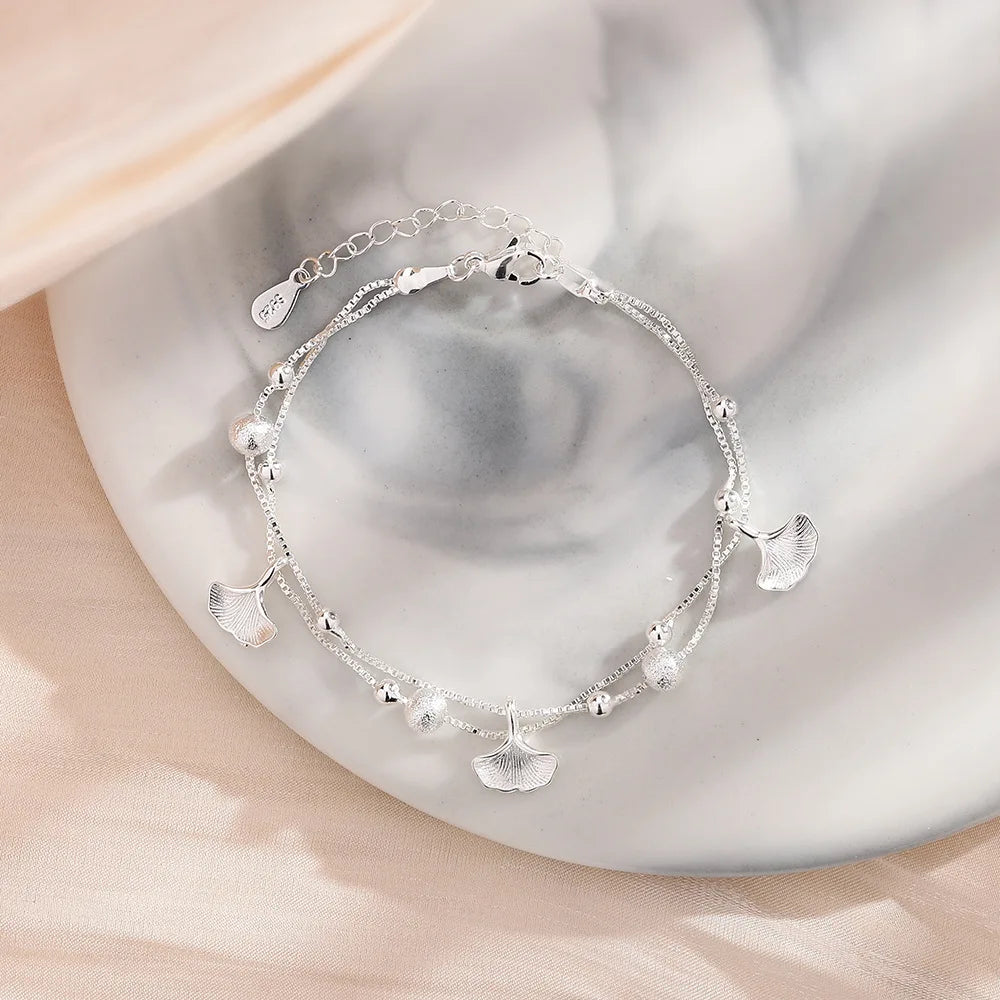 A sterling silver double heart charm bracelet is displayed on a white surface.