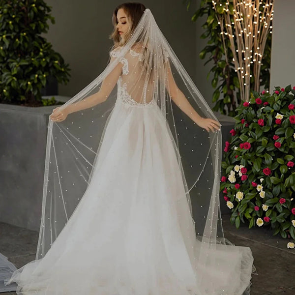 Une mariée en robe de mariage blanche et voile de perles transparentes dans un jardin.
