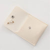 A light beige PU leather jewelry pouch with a snap button and a small pearl earring displayed on the interior.