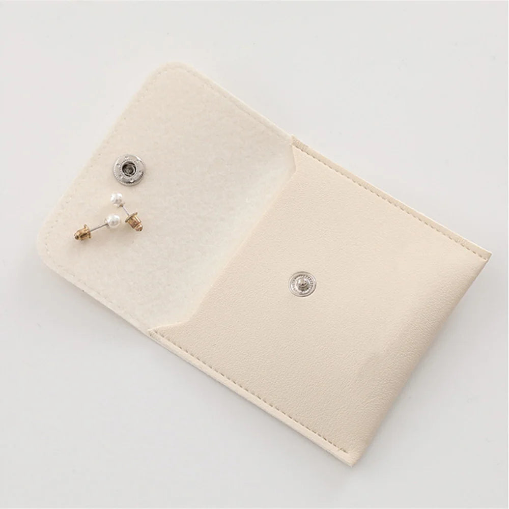A light beige PU leather jewelry pouch with a snap button and a small pearl earring displayed on the interior.