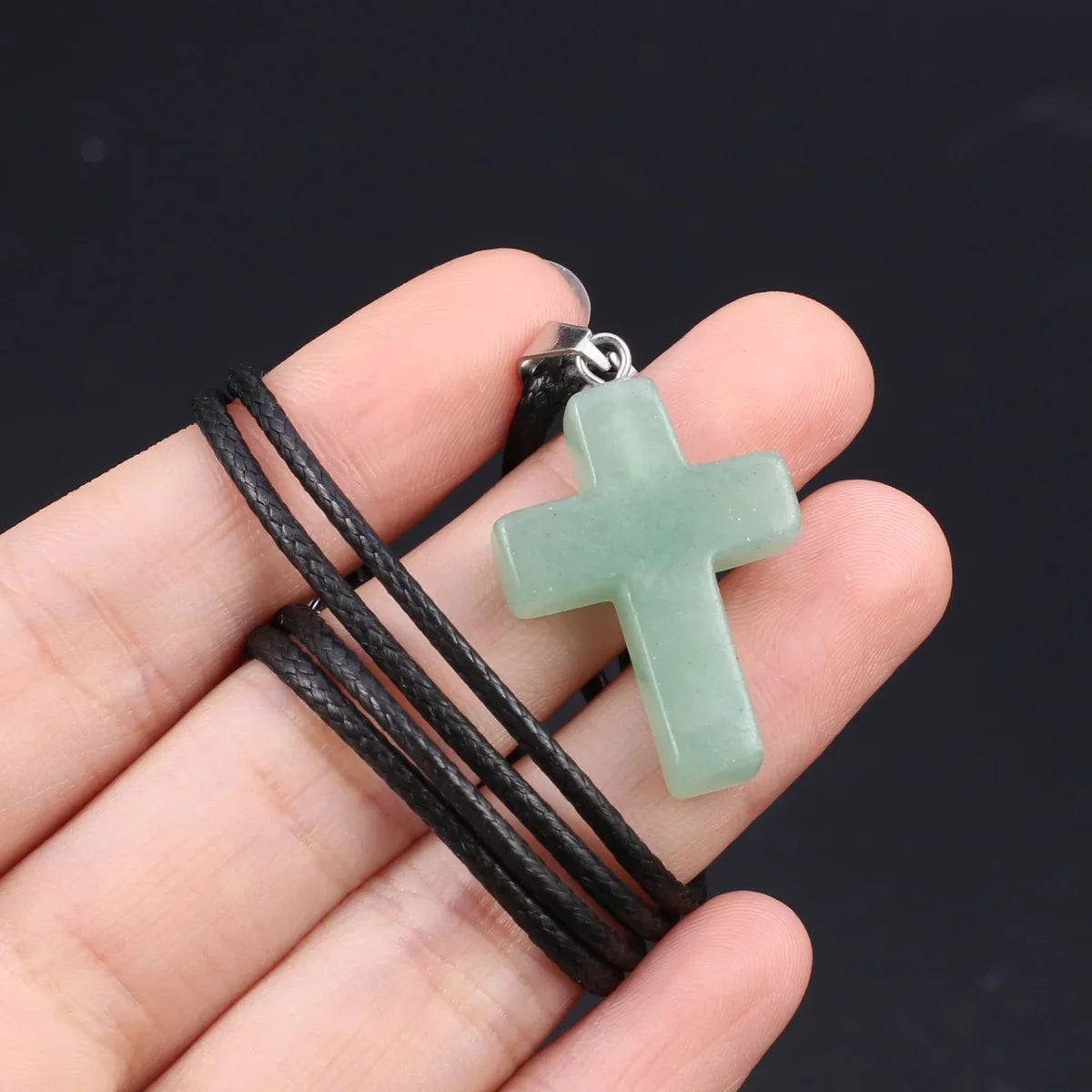 Eine Hand hält eine grüne Tigerauge-Agat-Kreuz-Anhänger-Kette mit schwarzem Band.