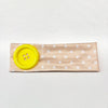 A beige fabric headband with white polka dots and a bright yellow button detail.