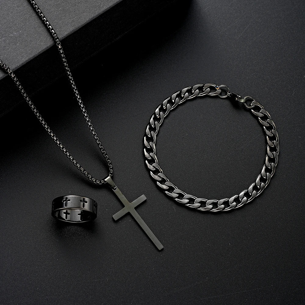 Un ensemble de bijoux en acier inoxydable pour homme, comprenant une chaîne, un pendentif croix et une bague, exposé sur une 