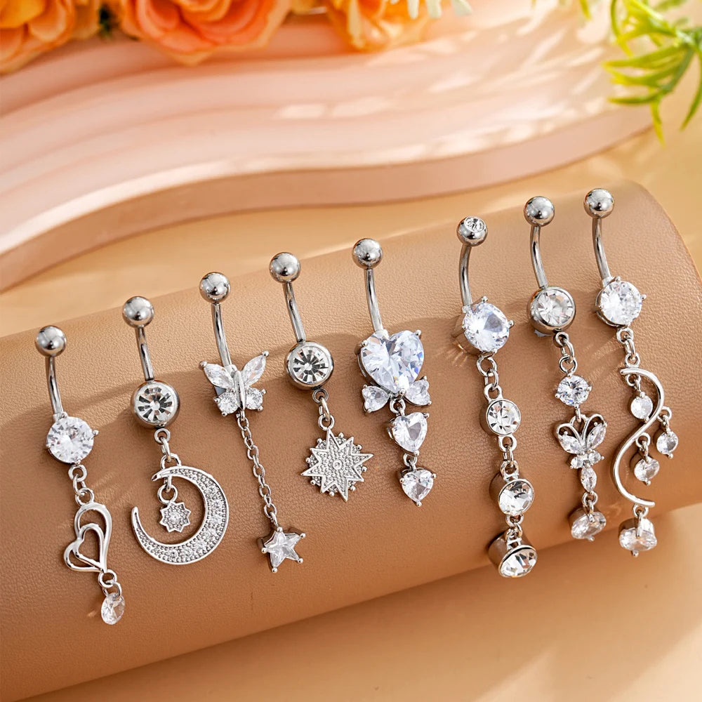A set of gold dangle curved belly piercing jewelry featuring heart, flower, and crescent moon charms.
