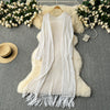A white knitted cardigan draped over a fluffy beige garment, set against a gray background with floral greenery.