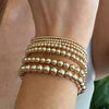 A stack of gold-toned round beaded bracelets worn on a wrist.