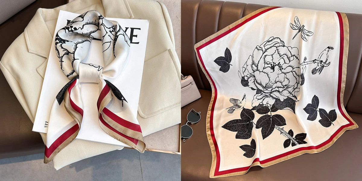 A cream silk scarf with a black floral print is displayed on a beige jacket and a brown leather sofa.