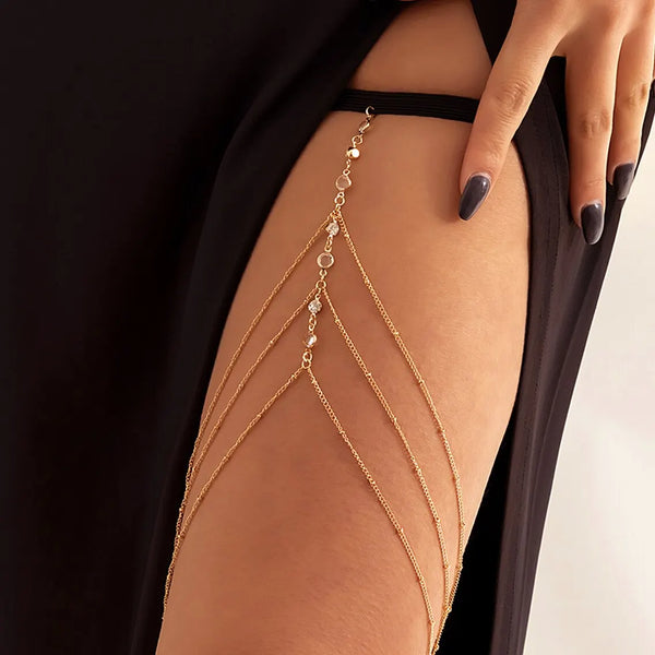 A close-up of a woman's leg adorned with delicate gold chain jewelry featuring small crystals and beads.