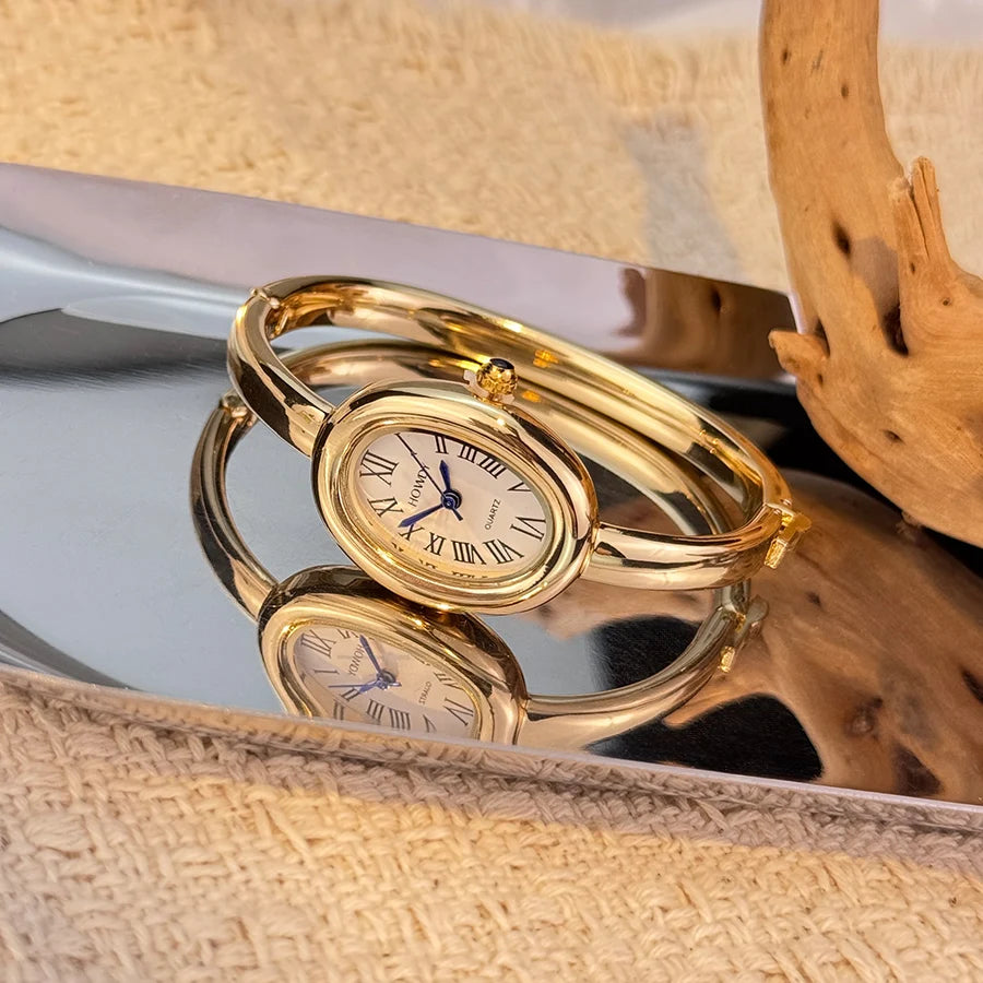 A pair of elegant gold-toned quartz watches with Roman numerals resting on a reflective surface.