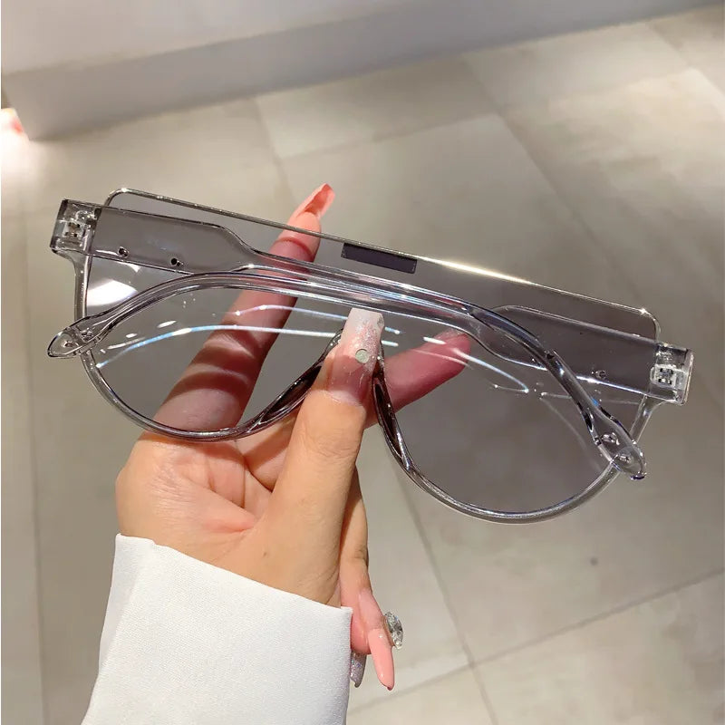A hand holds a pair of clear vintage cat eye sunglasses with UV400 protection against a light background.