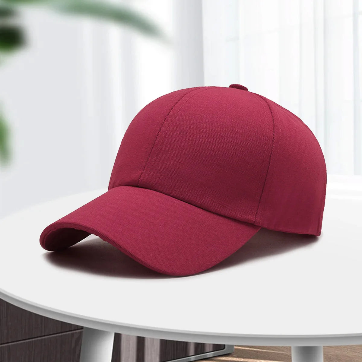 A maroon cotton curved visor hat is displayed on a white table.