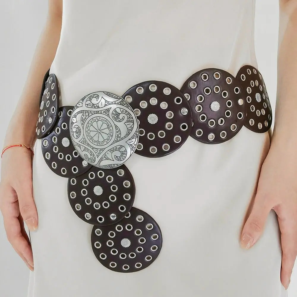 A close-up of vintage black PU disc belts with metal buckles worn on a white garment.
