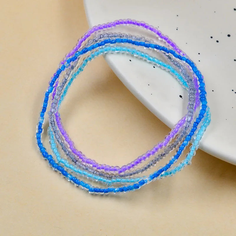 A collection of luminous glow-in-the-dark beaded anklets in shades of blue and purple displayed on a white surface.